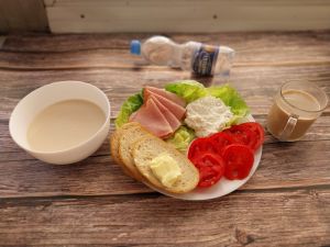 Zdjęcie przedstawia Dietę podstawową:  Płatki jęczmienna na mleku Chleb mieszany pszenno-żytni Masło extra  Kawa zbożowa z mlekiem Szynka Piastowska- wp., wędzona, parzona z dod. b.sojowego i wody Woda mineralna Sałata zielona Pasta z twarogu z natką pietruszki Pomidor